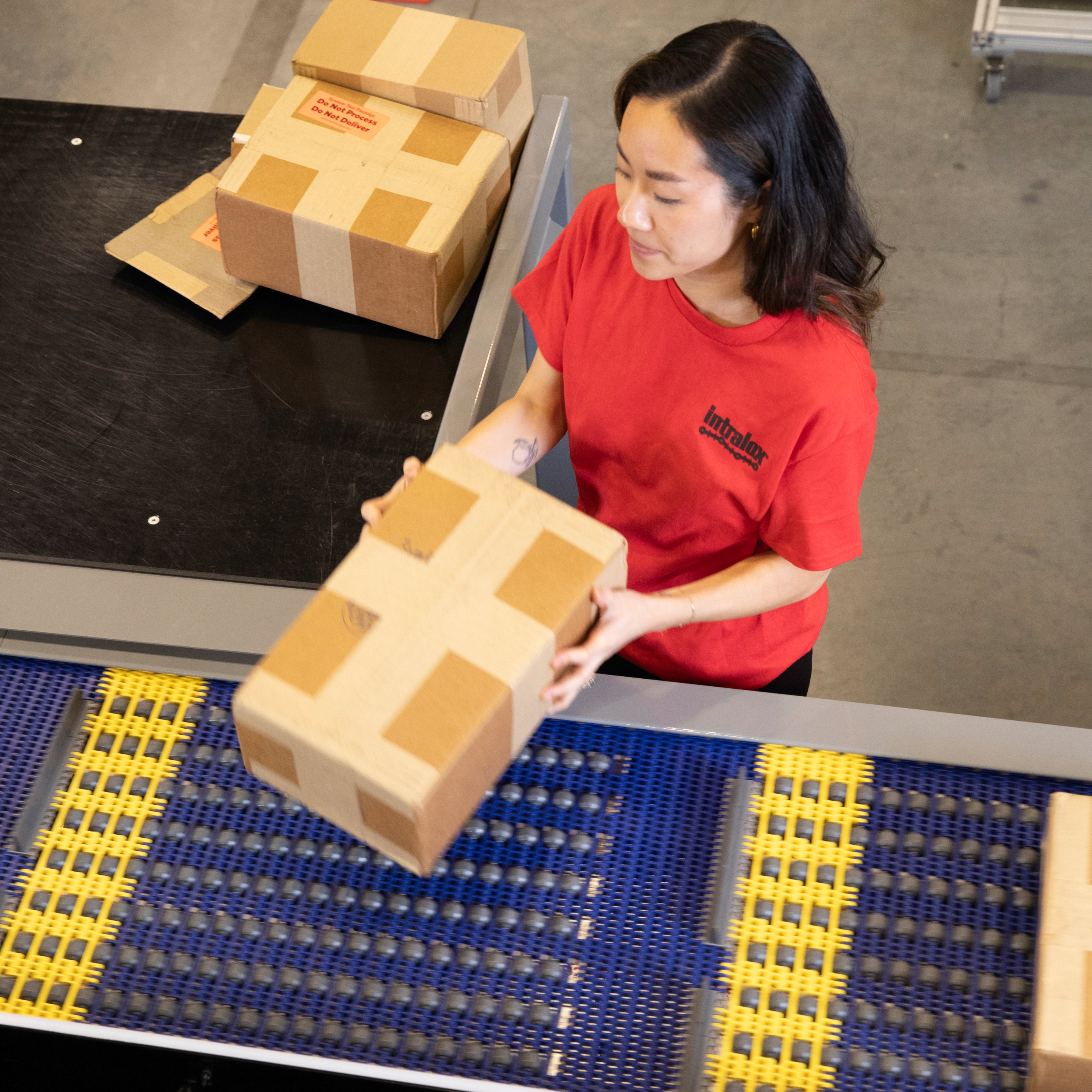 身穿红色 T 恤的女操作员正在将包裹放到 ARB AutoPitch 供包台设备上