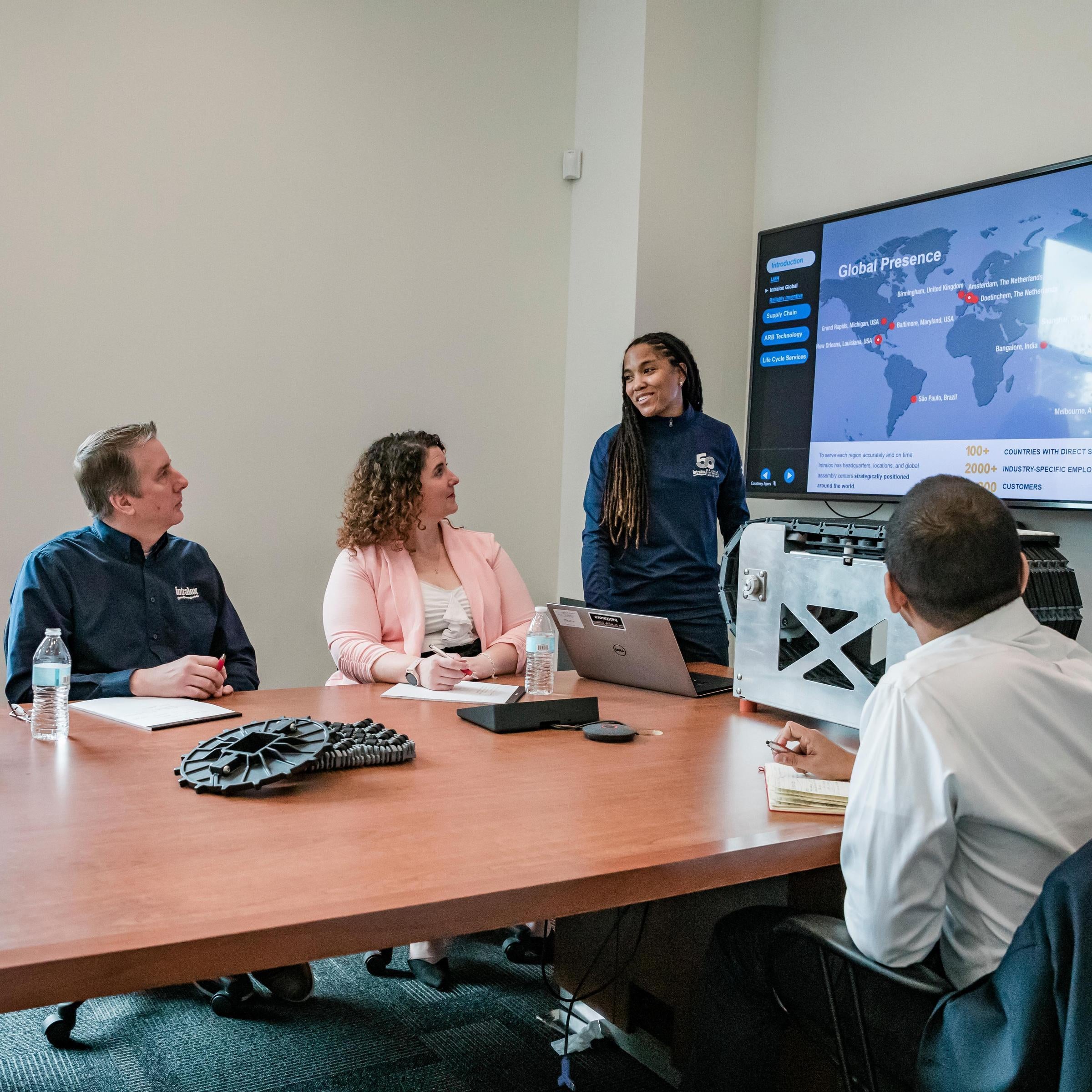 People in a boardroom watching a woman present on a television screen