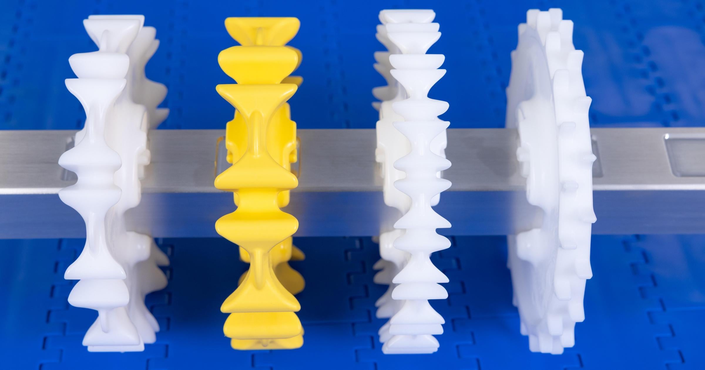 Four CleanLock sprockets of differing size, shape, and color mounted on a CleanLock shaft with blue conveyor belt in background