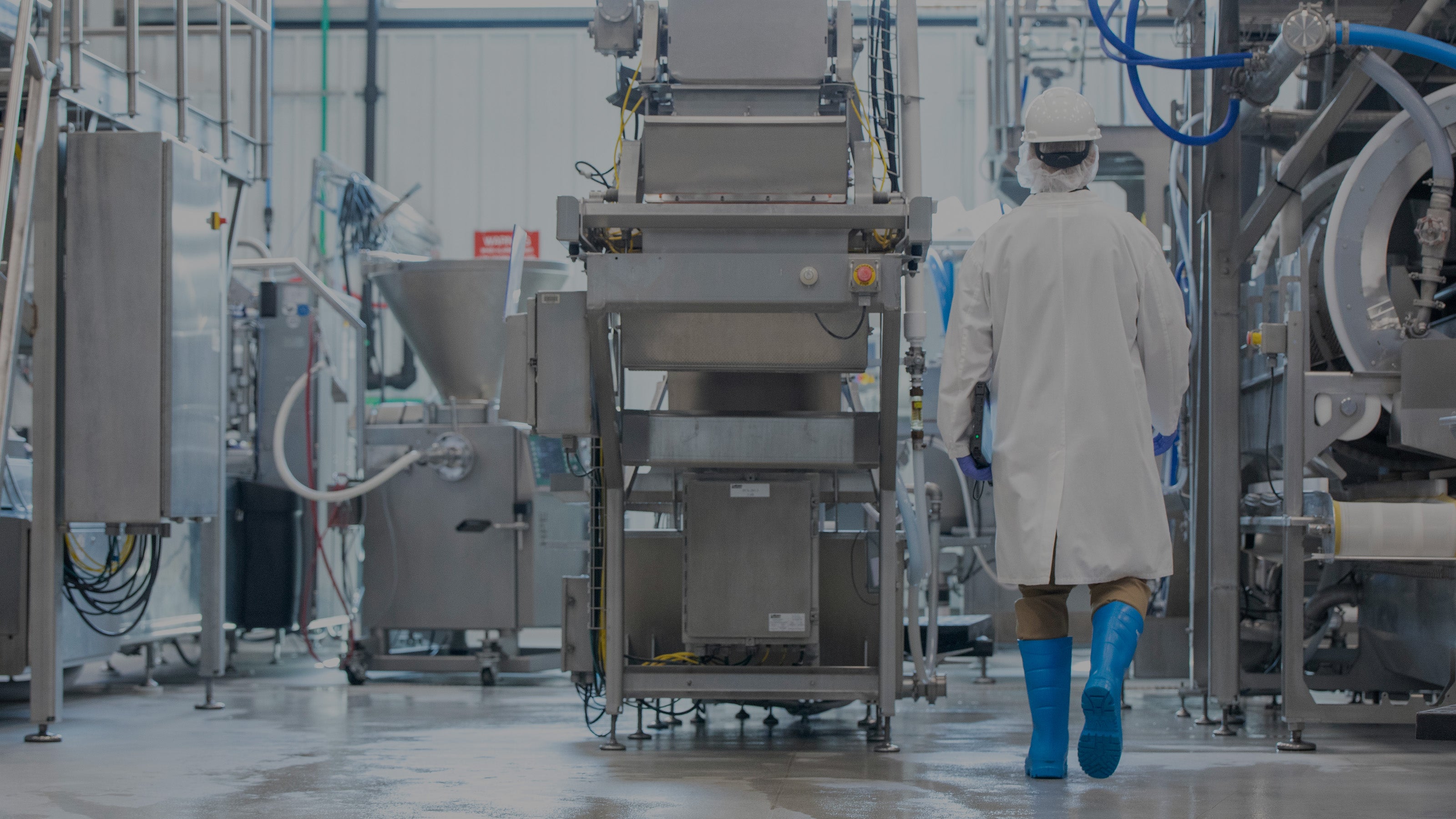 穿戴白色防护装备的操作人员朝着制造设备走去，图片调暗了 35%