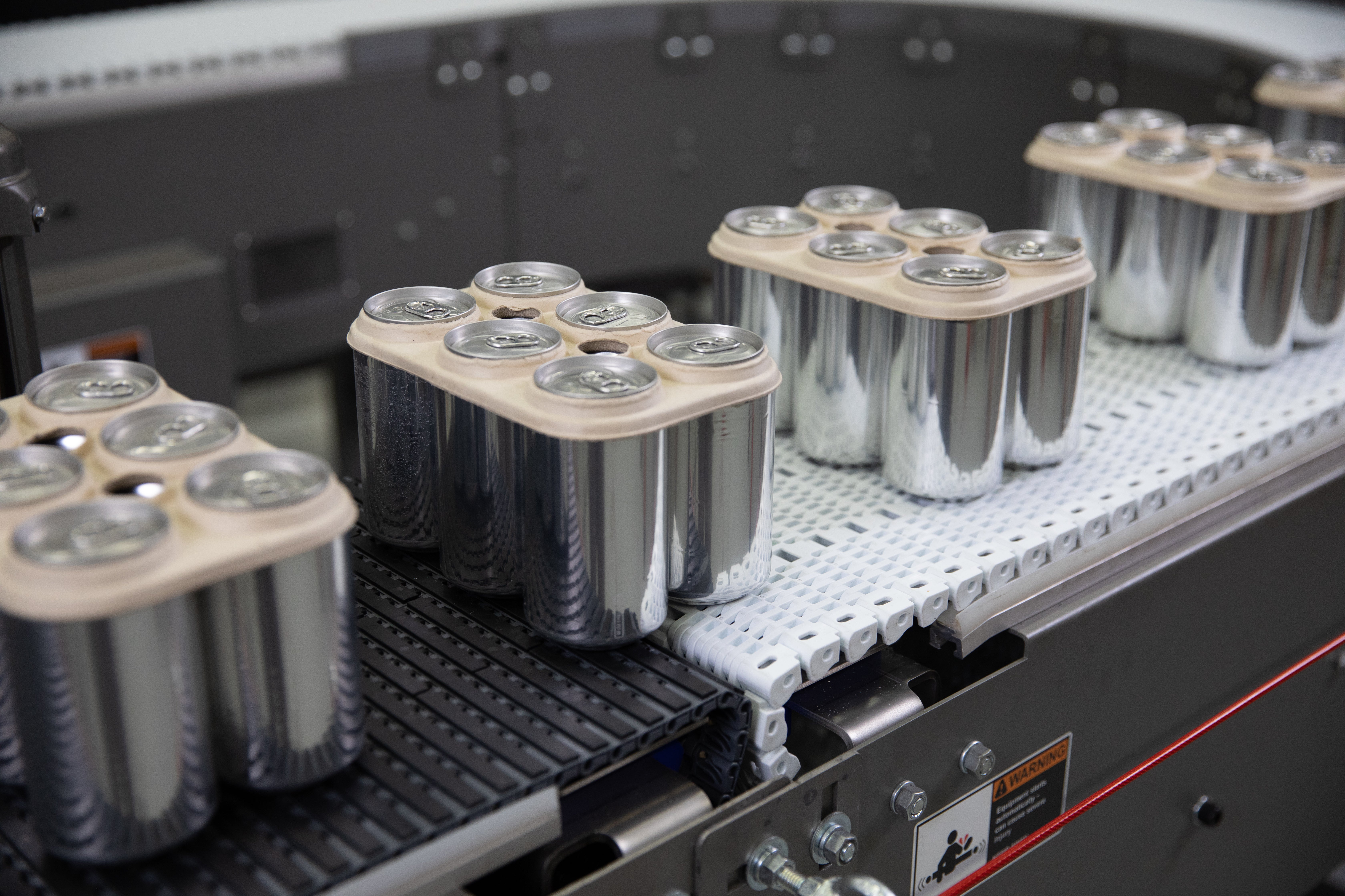 Packs de seis latas de aluminio empaquetados con anillos de cartón que se mueven por la transferencia