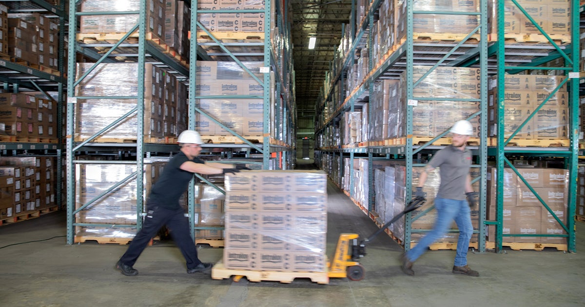 Two workers use a pallet truck to move boxes in a warehouse