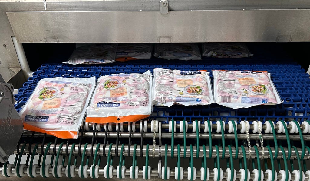 Bagged imitation crab meat exits Trans-Ocean Products's new, Intralox MPB spiral onto a plastic conveyor belt.