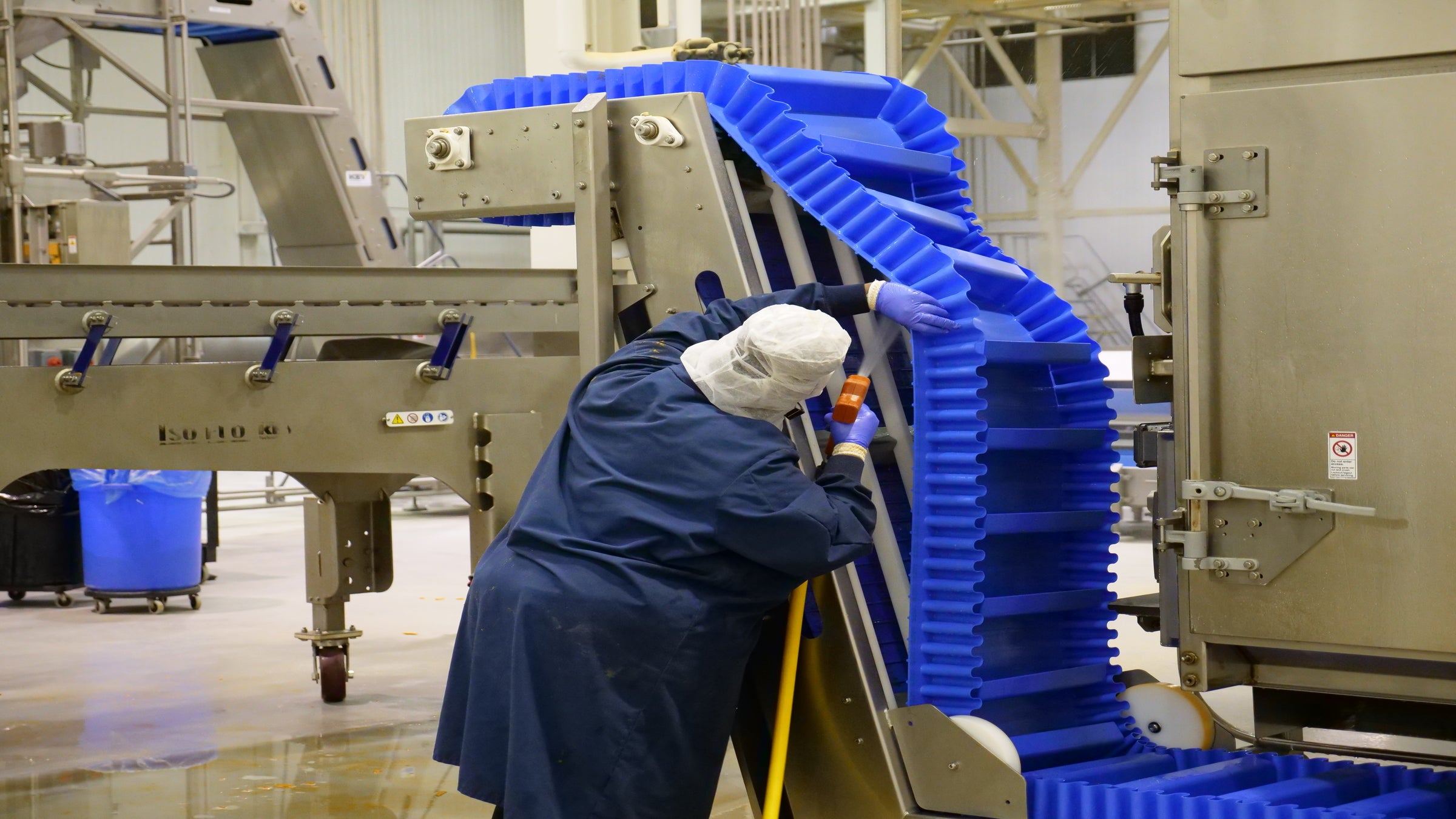 Trabalhador limpando a parte inferior da esteira transportadora inclinada ThermoDrive A23 com conchas e paredes laterais