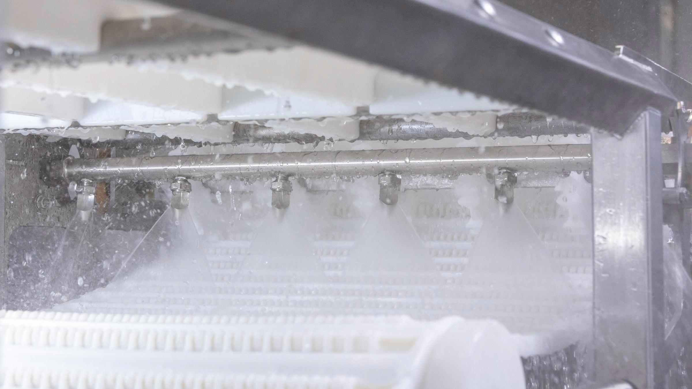 Barra com pulverizadores de água para limpeza no local da Intralox pulverizando água na esteira transportadora branca