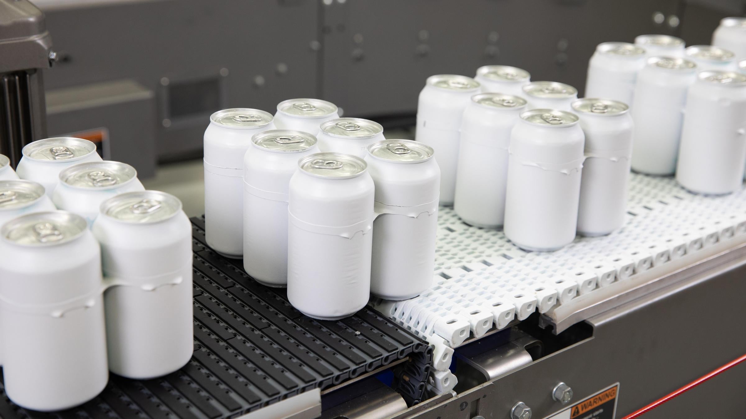 6個パックのアルミニウム缶と白い空白の包装機を、白色の曲線コンベアベルトからレイズドリブ付きの灰色のコンベアベルトに搬送する