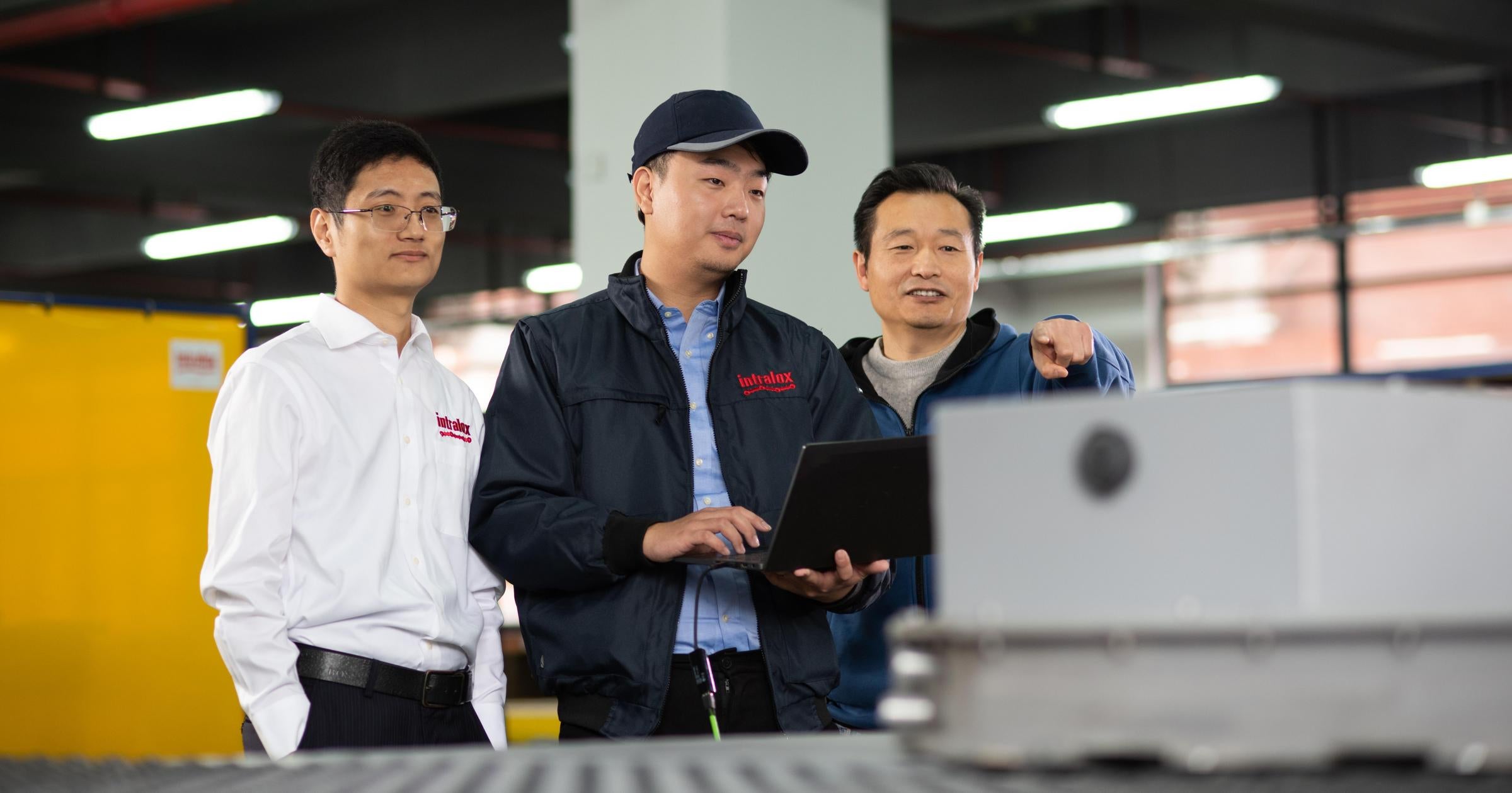 Tre uomini che guardano una batteria EV su un trasportatore DARB. Uno la indica e l'altro tiene un laptop e indossa un berretto con visiera.