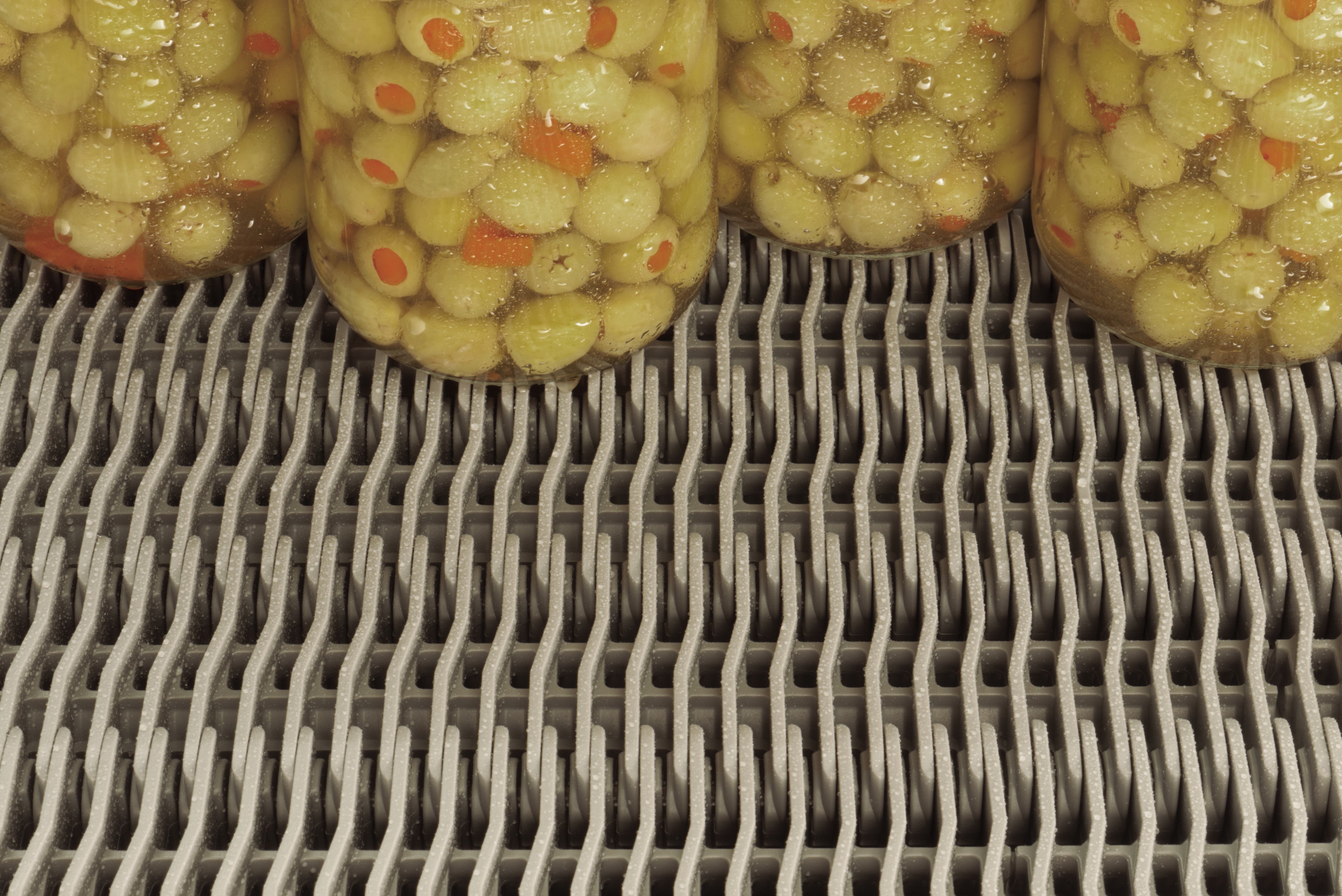 Jars of canned green olives on Raised Rib pasteurizer belt