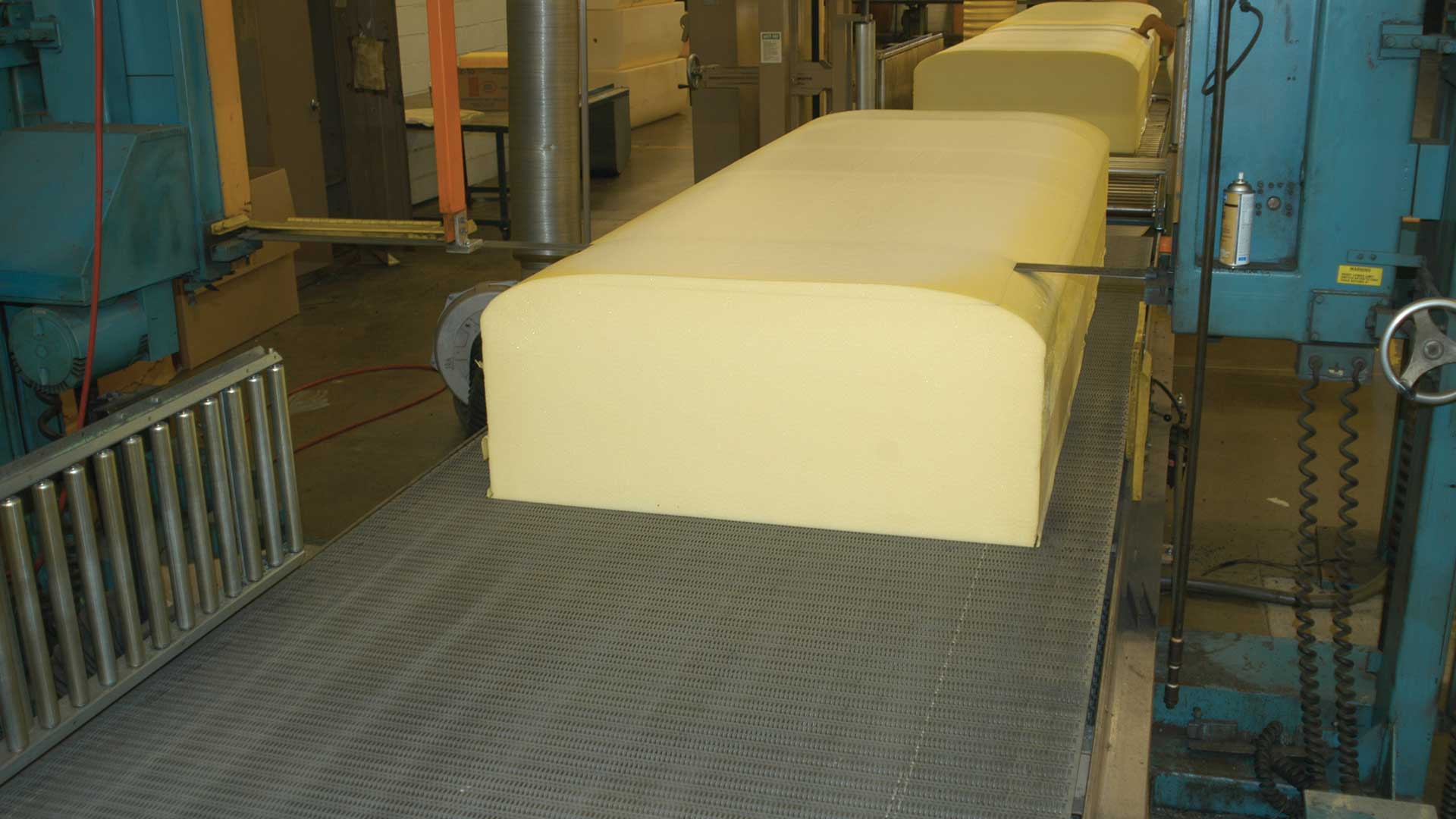 Barra grande de espuma de poliuretano que está siendo cortada por una máquina