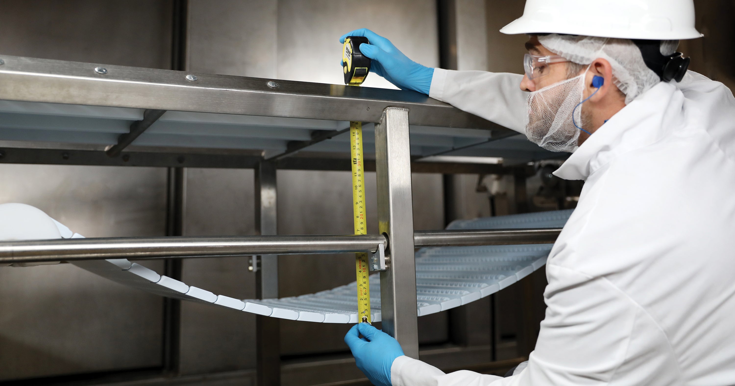 Worker measuring conveyor belt catenary sag on a conveyor