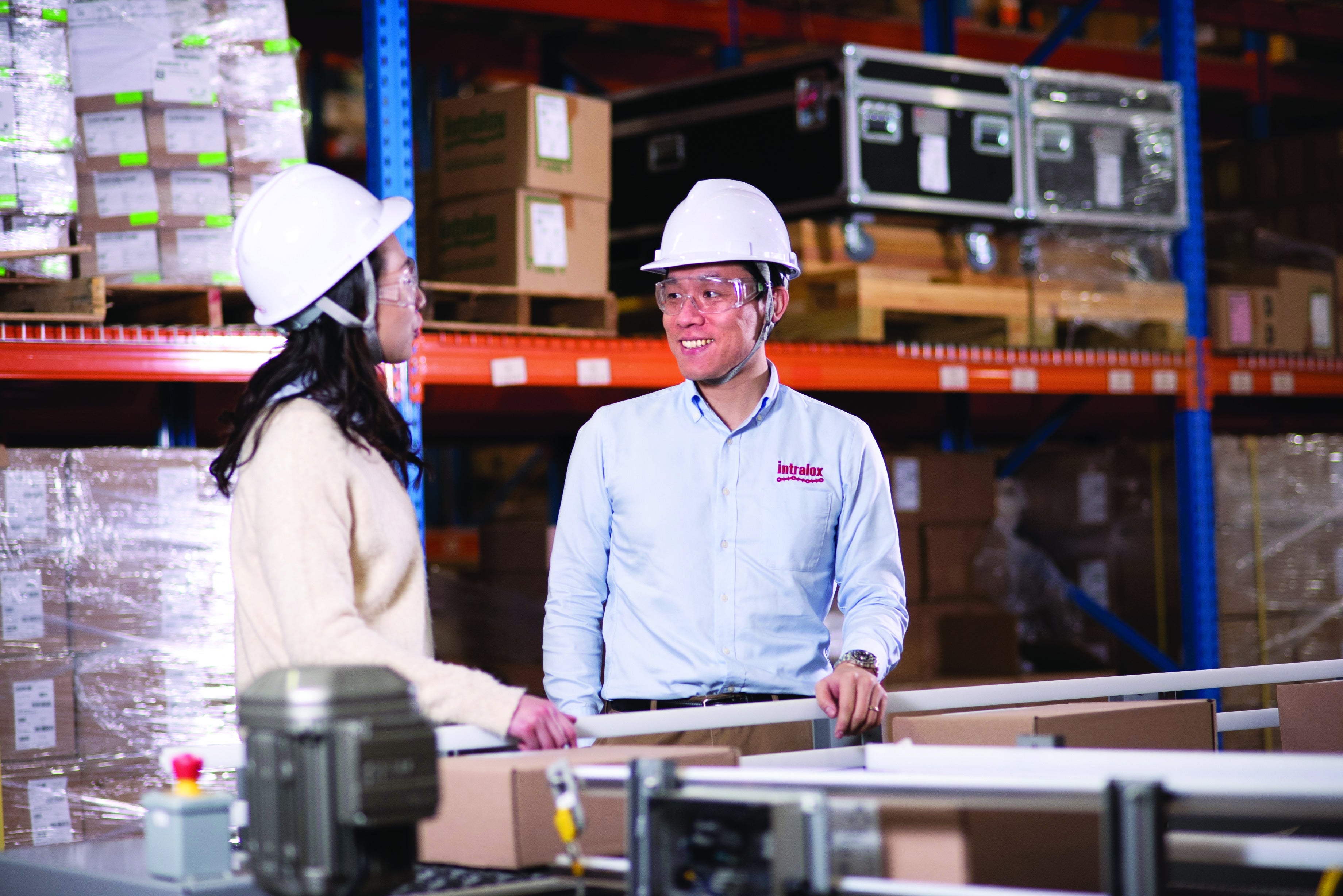 Hombre y mujer con cascos parados junto a transportadores en el almacén