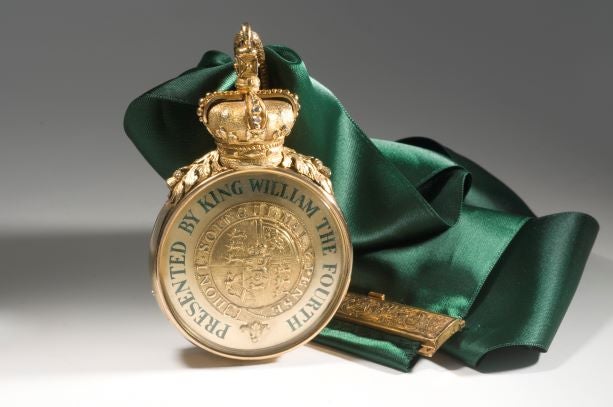 King William IV Royal Medal of The Royal and Ancient Golf Club of St Andrews. Gold medal with a gold crown and leaves at the top. Green writing says, "Presented by King William the Fourth". Green, silk ribbon.