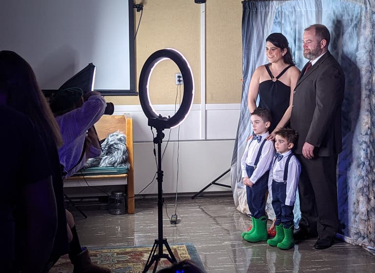 A family in formal wear, two young boys in suspenders and green rain boots, poses at the photo booth.