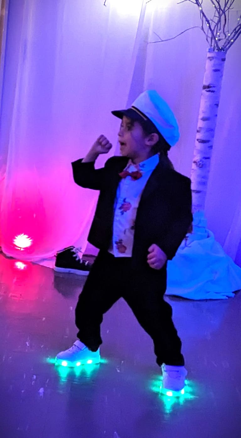 A young boy in a tuxedo jacket, bow tie and captain's hat strikes a dance pose in glowing sneakers.