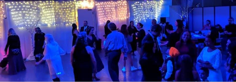 Packed hall of dancing people of all ages in a space lit with fairy lights.