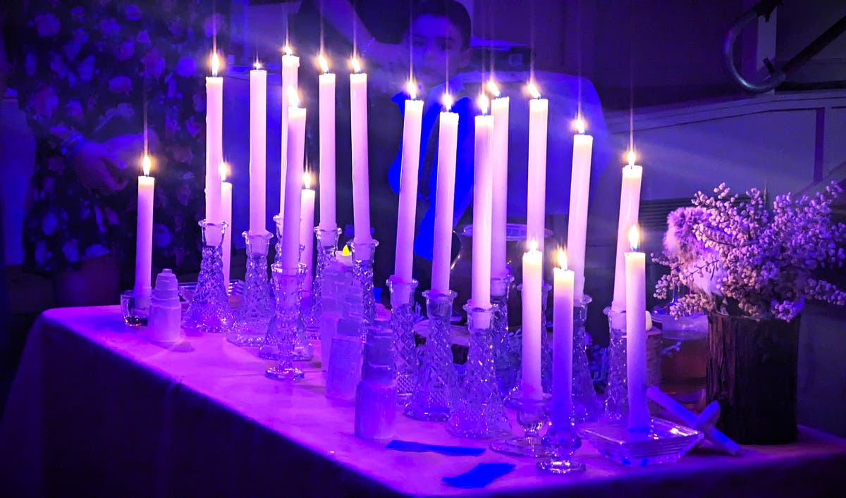 Rows of lit white taper candles in crystal holders on the ritual table, beside a vase of small white flowers.