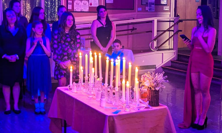 Guests of all ages watch the candle-lighting ritual around a table of tall white candles.
