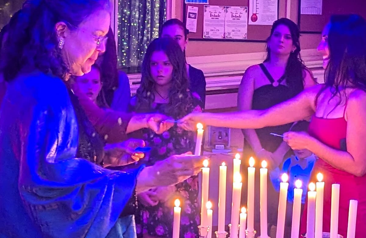 Guests of all ages gather at the candle table as an older woman lights a taper and others reach in to light theirs.