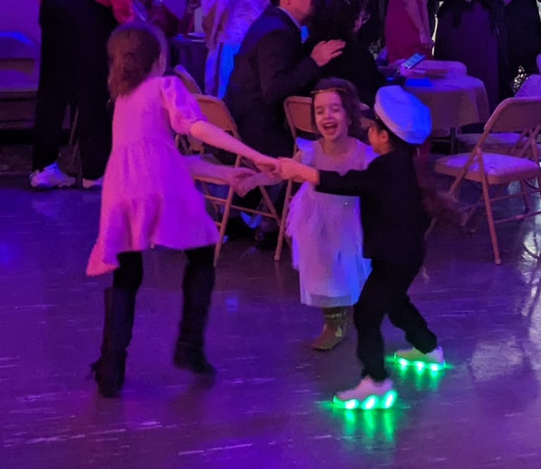 Children hold hands and spin in a circle on the dance floor, laughing.