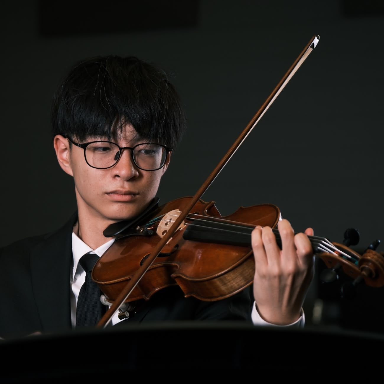 Black-haired man with glasses and in a suit plays the violin while standing