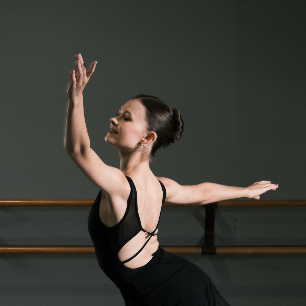 Ballerina dressed in black dress dancing in a well lit studio room