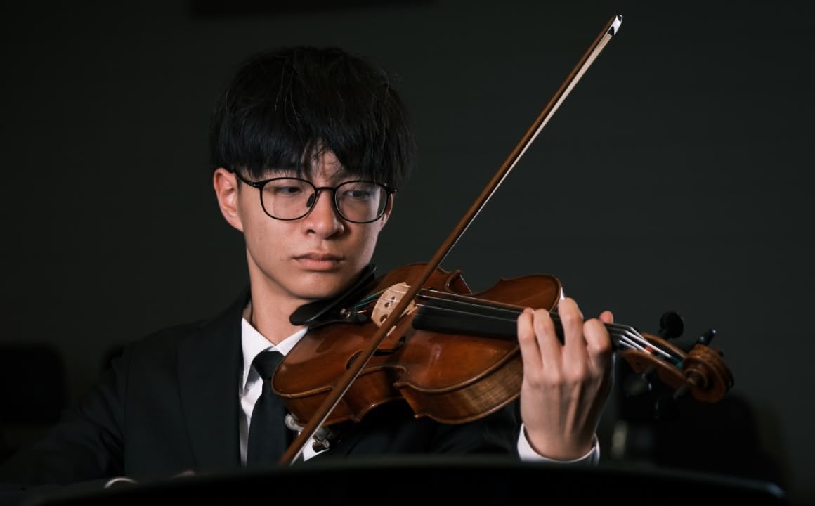 Black-haired man with glasses and in a suit plays the violin while standing