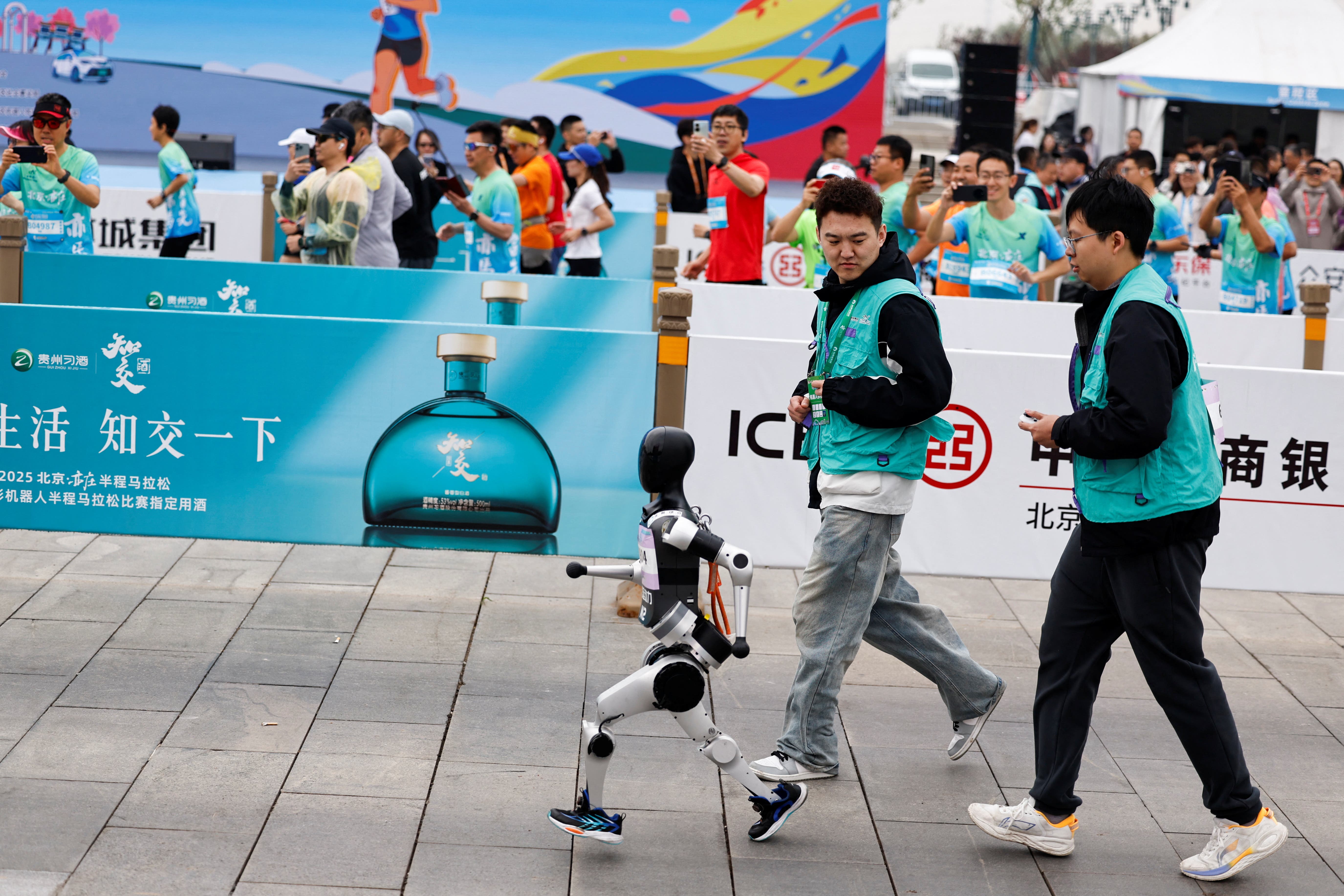 Engineers run with the humanoid robot "Noetix N2" as it participates along with human runners in the E-Town Half Marathon & Humanoid Robot Half Marathon in Beijing, China April, 19 2025. REUTERS/Tingshu Wang
