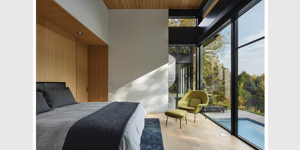 Interior view of master bedroom with floor to ceiling windows, looking out to pool