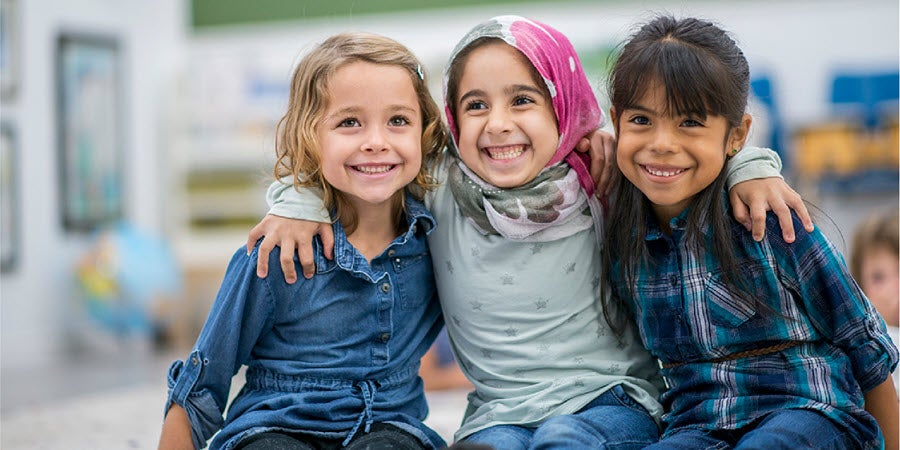 Three young girls with arms around each other smiling 
