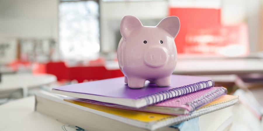 1987 School Cash Management - photo of a pink piggy bank on top of a stack of purple, pink and yellow spiral notebooks
