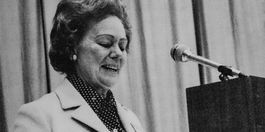 grainy black and white photo of a woman giving a speech in front of a microphone