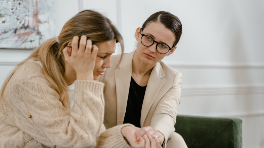 photo of a woman wearing glasses holding the hand of another woman in distress