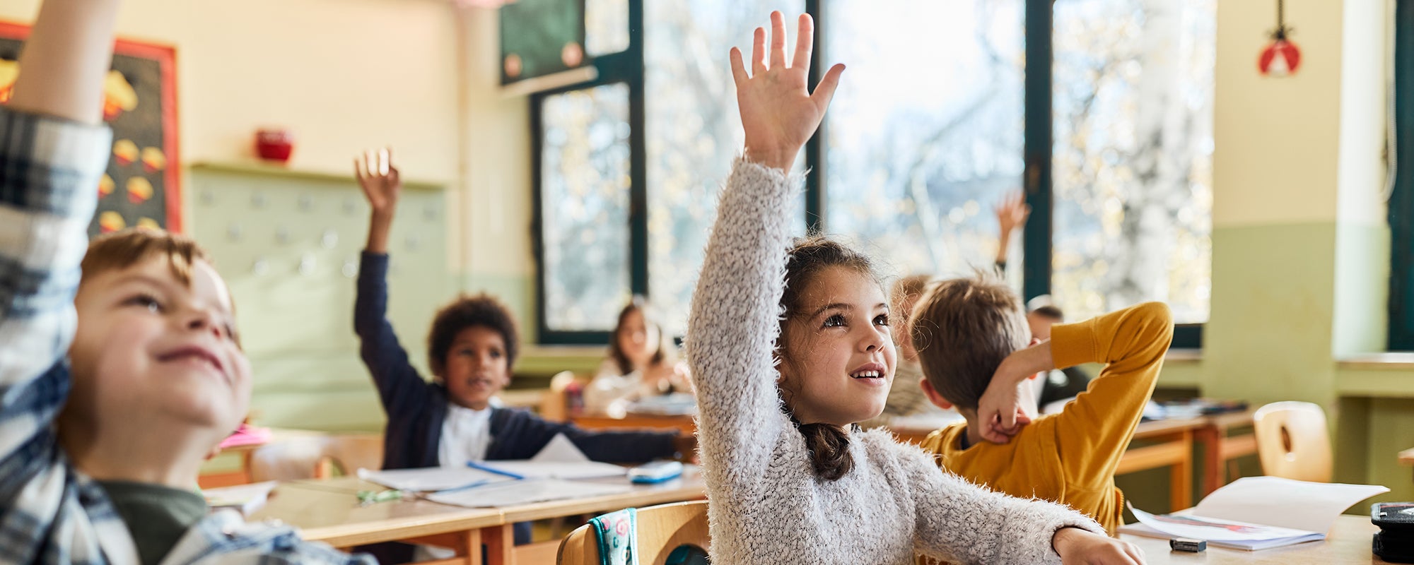 Happy schoolgirl and her friends raising hands on a class.
