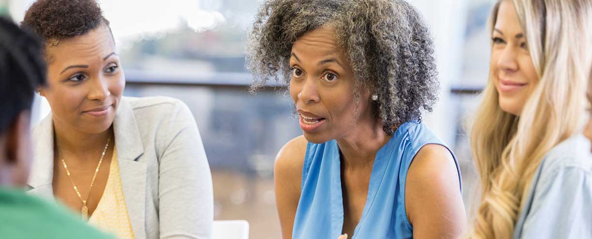 A woman talks in a meeting while colleagues look on.