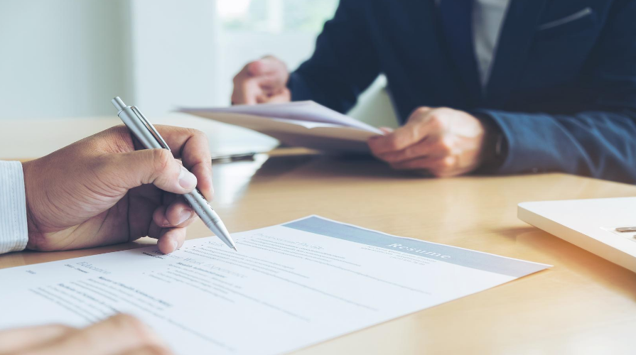 Hand holding pen reviewing document across the table from another set of hands holding documents