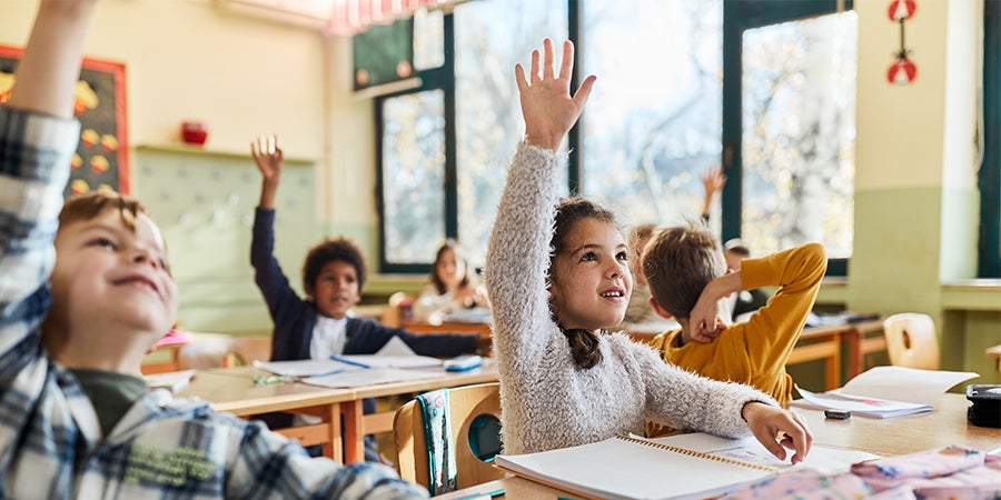 Happy schoolgirl and her friends raising hands on a class.
