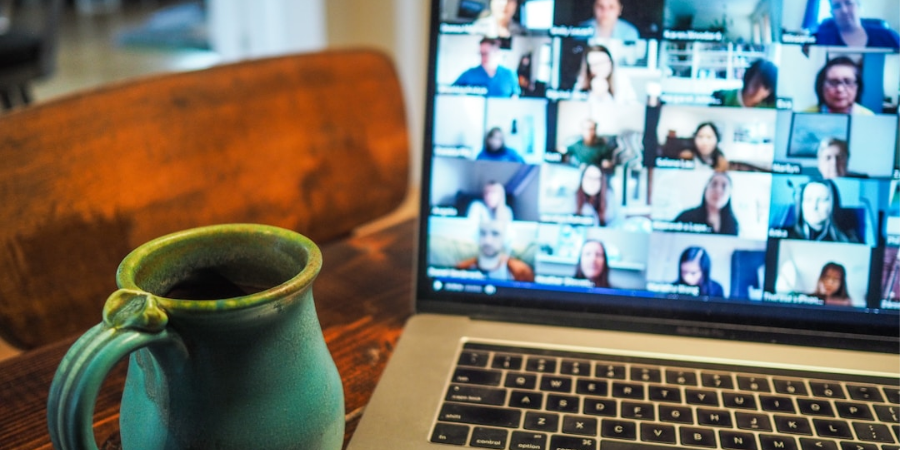 Image of laptop open with a video conference call displayed on the screen. Coffee mug in the foreground.