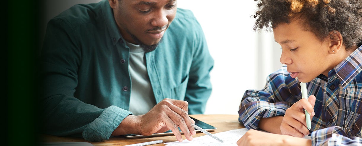 A parent and student sitting at a table with the parent helping the child with homework.