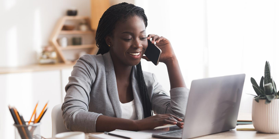 Woman in professional attire smiling while talking on cell phone and using a laptop