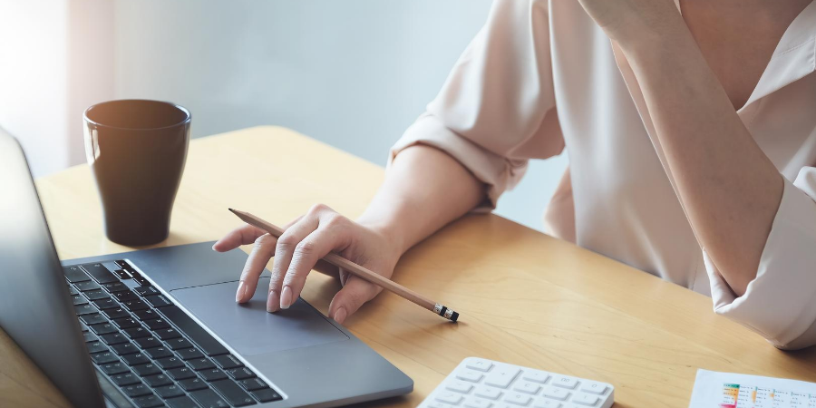 Image of hand using laptop touch pad and holding a pencil