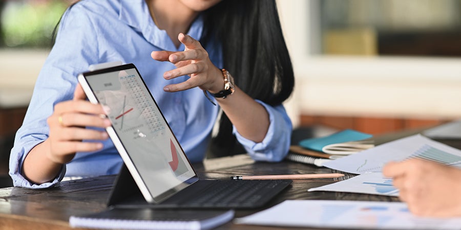 photo of a woman dressed in a blue blouse holding a tablet screen displaying graphs and charts 900x450px