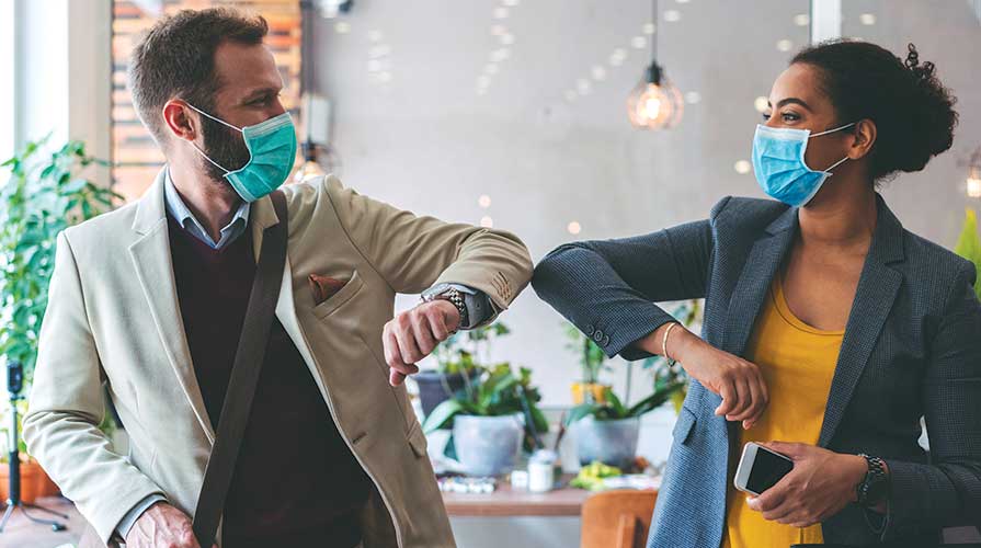 Two workers bumping elbows instead of high-fiving, both with masks on.