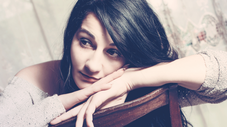 A woman with a sad expression leaning on the back of a chair.