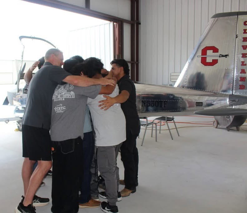 Students and teacher huddling in front of plane.