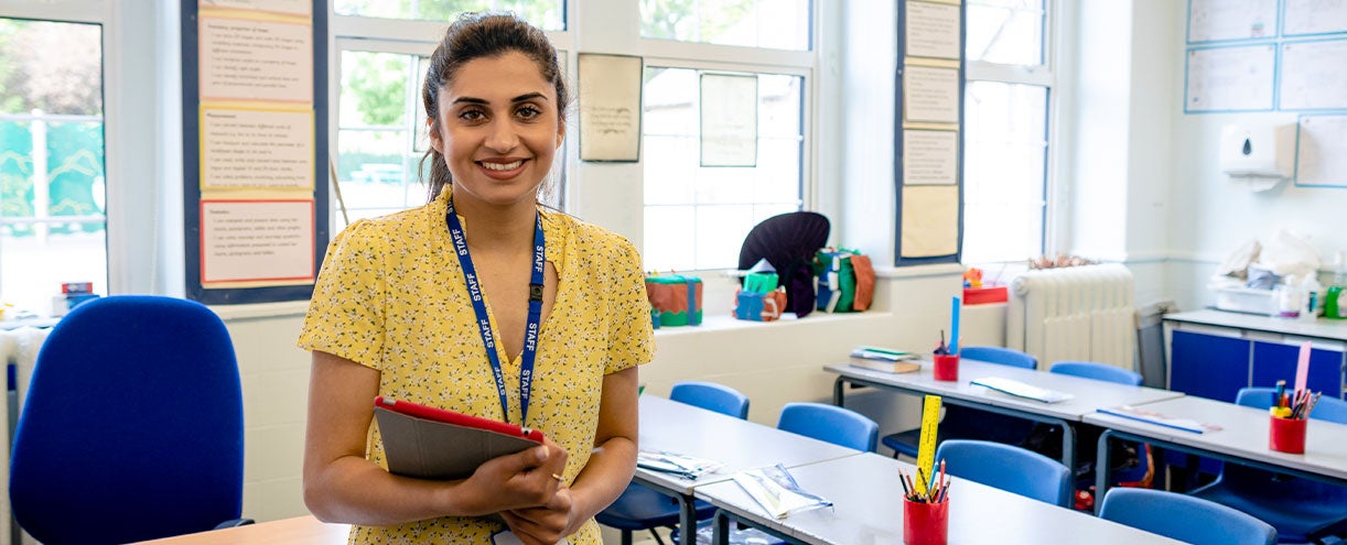 A young teacher stands in an empty classroom.
