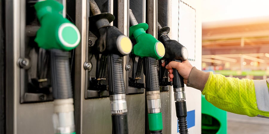 Person with yellow sleeve reaching for fuel pump handles.