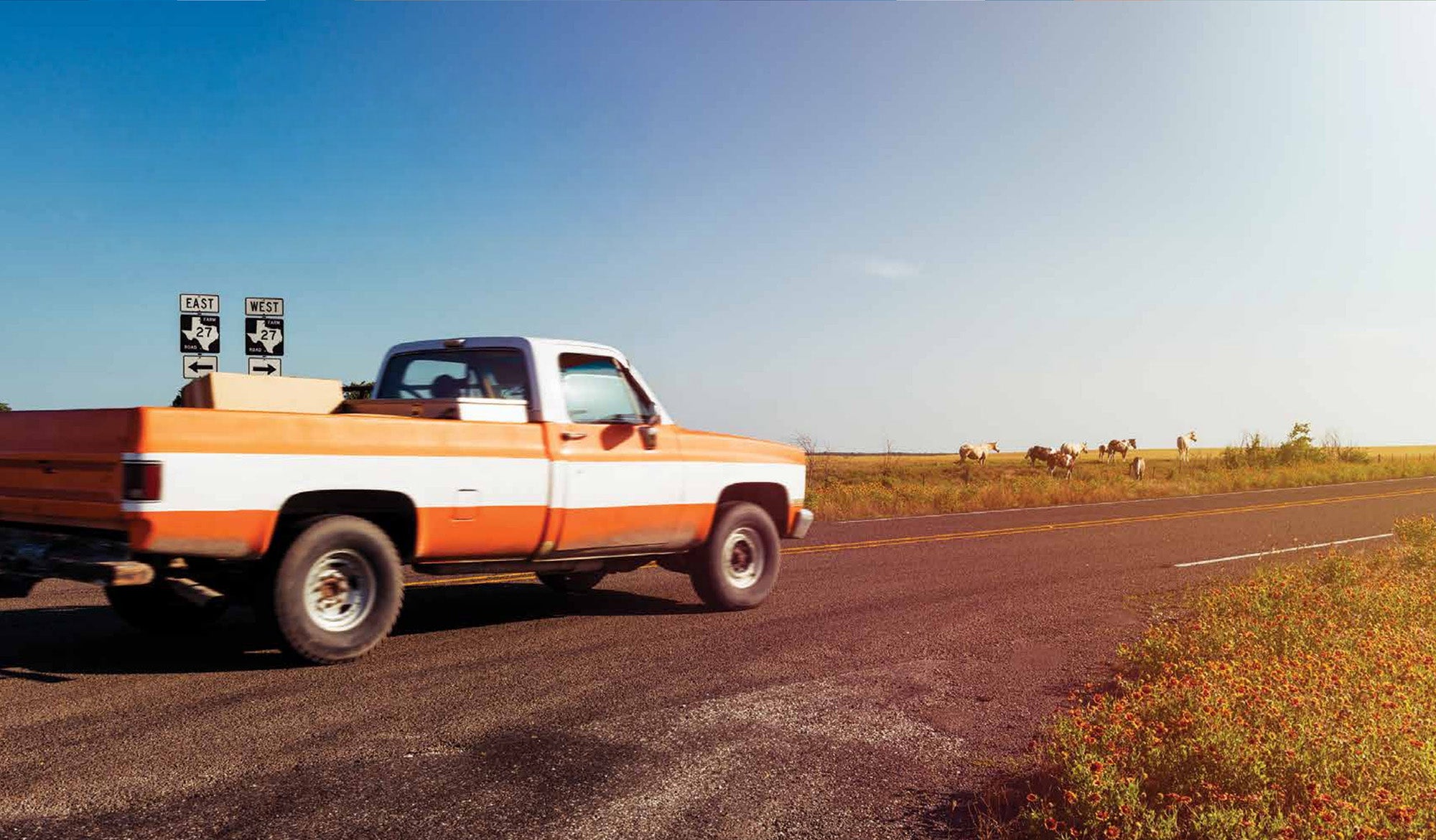 Orange truck driving down a farm road