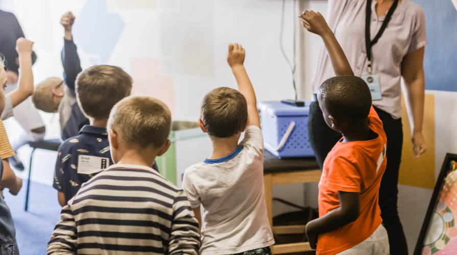 photo of classroom of pre-k students raising their hands