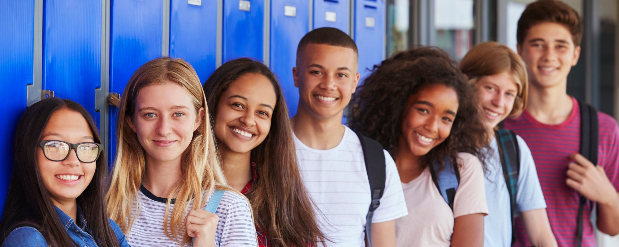 Group of students smiling and standing in front of lockers