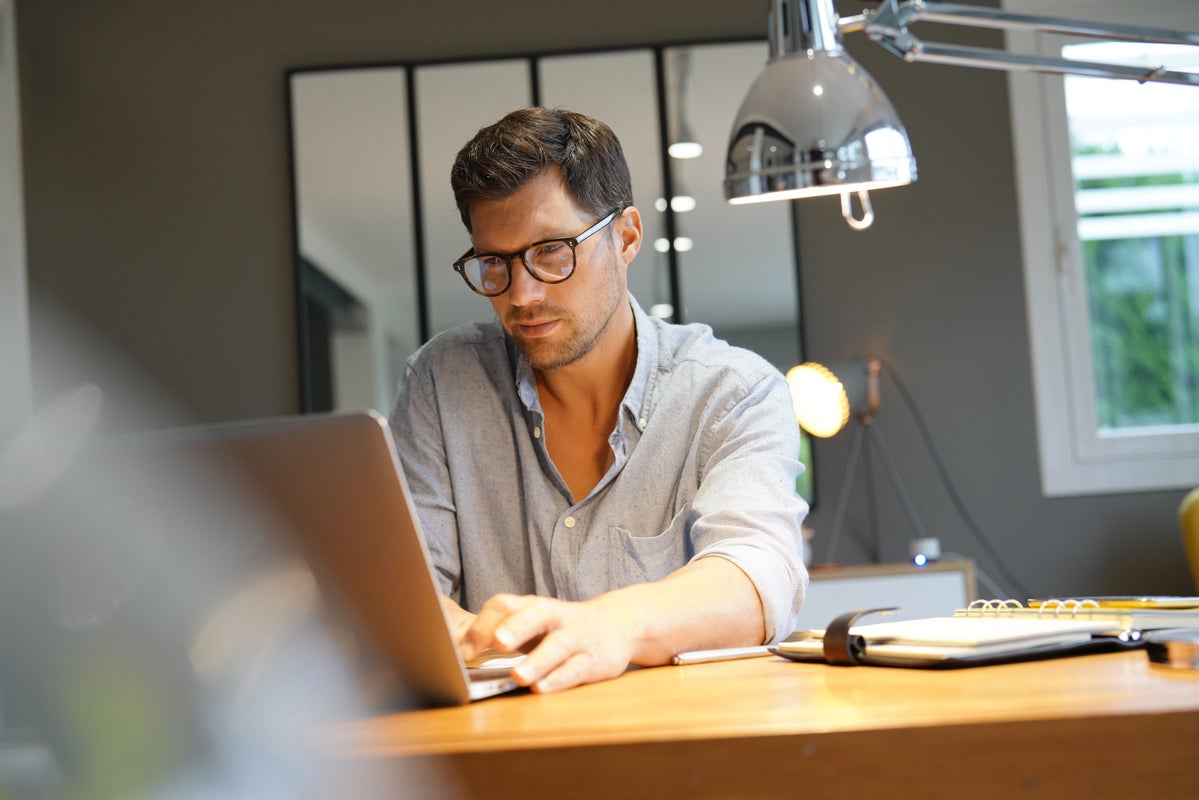 Man with glasses working at a laptop.